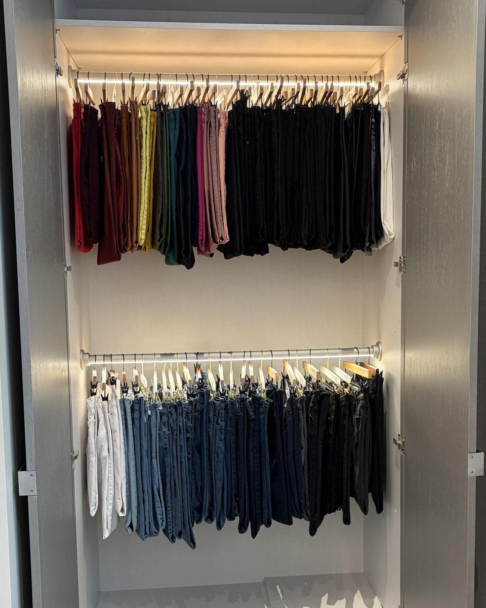 A wardrobe of trousers and jeans hung on matching hangers and sorted by colour